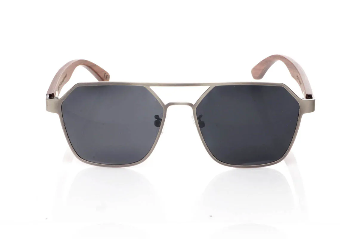 Gafas de Madera Natural de Walnut IBON. Las gafas de sol <b>IBON</b> combinan un frontal metálico de líneas geométricas con varillas de madera de walnut, creando una mezcla sofisticada entre diseño moderno y calidez natural. Su forma angular, con doble puente abierto y estructura ligera al aire, aporta un estilo atrevido y muy actual, ideal para quienes buscan unas gafas con presencia sin resultar pesadas. Las varillas de madera, finas y curvadas, muestran vetas naturales que hacen que cada par sea único y aportan comodidad durante el uso diario. Equipadas con lentes polarizadas que reducen los reflejos y protegen eficazmente frente a los rayos UV, son unas gafas diferentes, elegantes y con carácter propio. Medidas: 145x50 mm. Calibre 54. Venta al Por Mayor y Detalle | Root Sunglasses® 